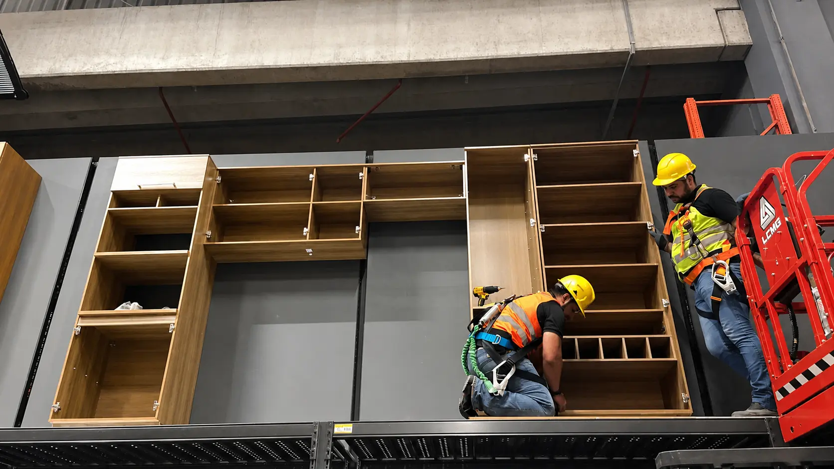 Equipe CLT da PDV Constru com capacete, colete refletivo e cinto de segurança instalando mostruário em altura, com plataforma elevatória