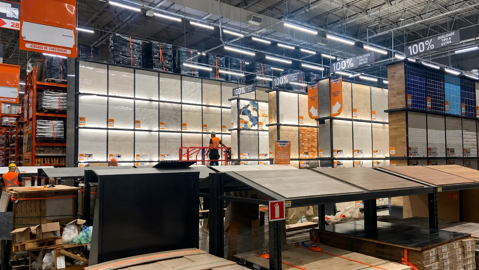 Mostruário cerâmico da PDV Constru instalado em Home Center, com painéis backlit e operário montando o display em plataforma elevatória